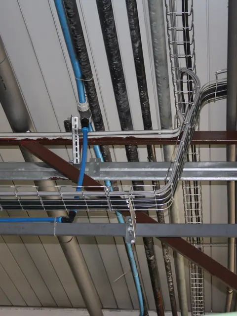 Eletrocalhas e leitos de cabos fixados no teto de uma instalação